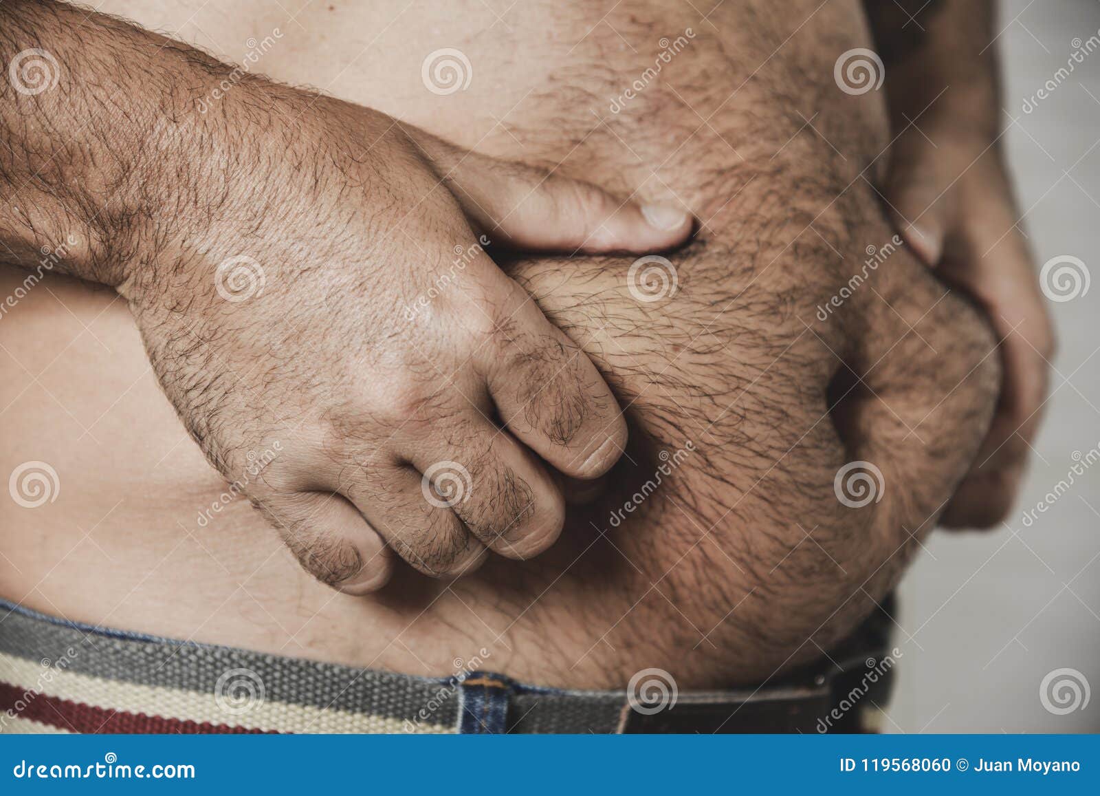 Closeup of a caucasian man grabbing the fat of his hairy stomach.