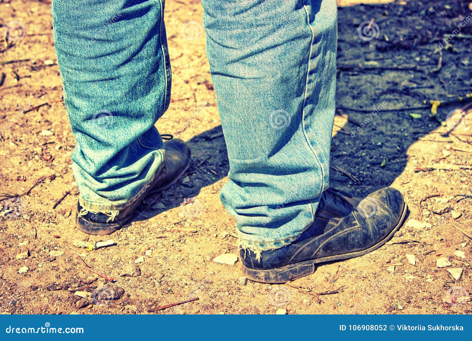 Closeup of feet of a man in old blue jeans and worn-out shoes. Tinted