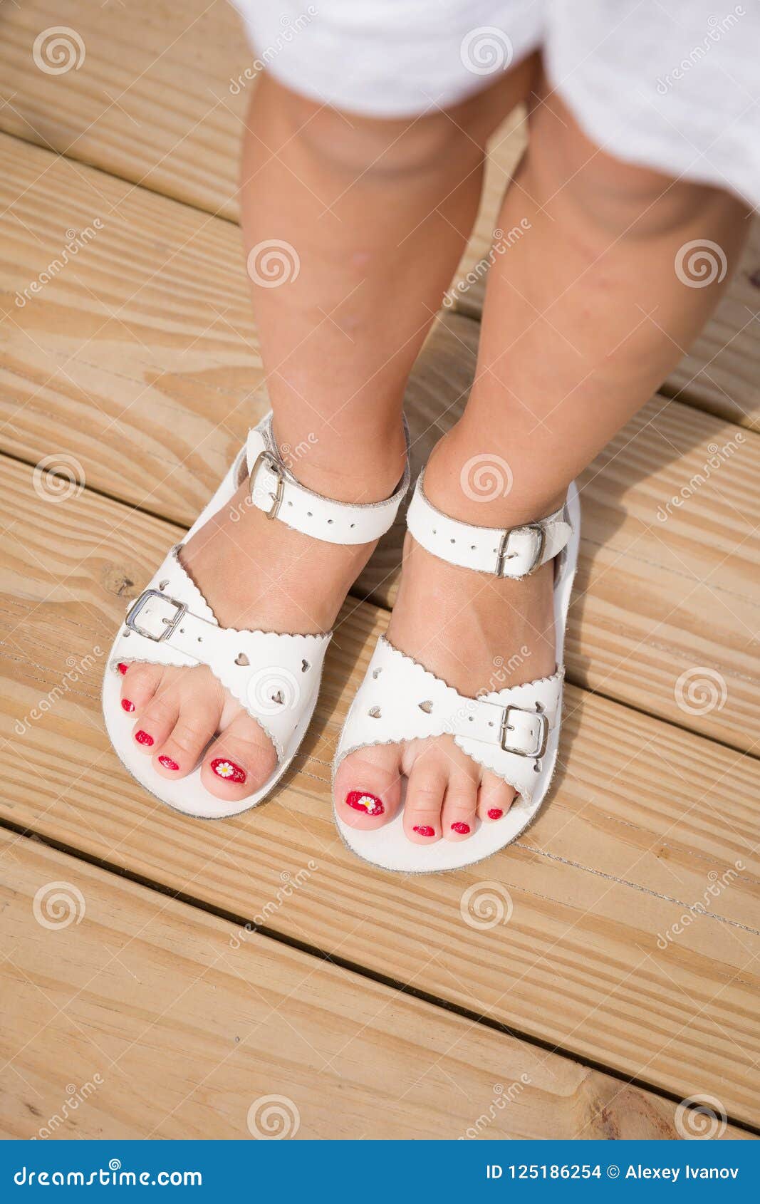 closeup of girl`s feet in white sandals on the wooden floor. funny red nails. summer time. vacations