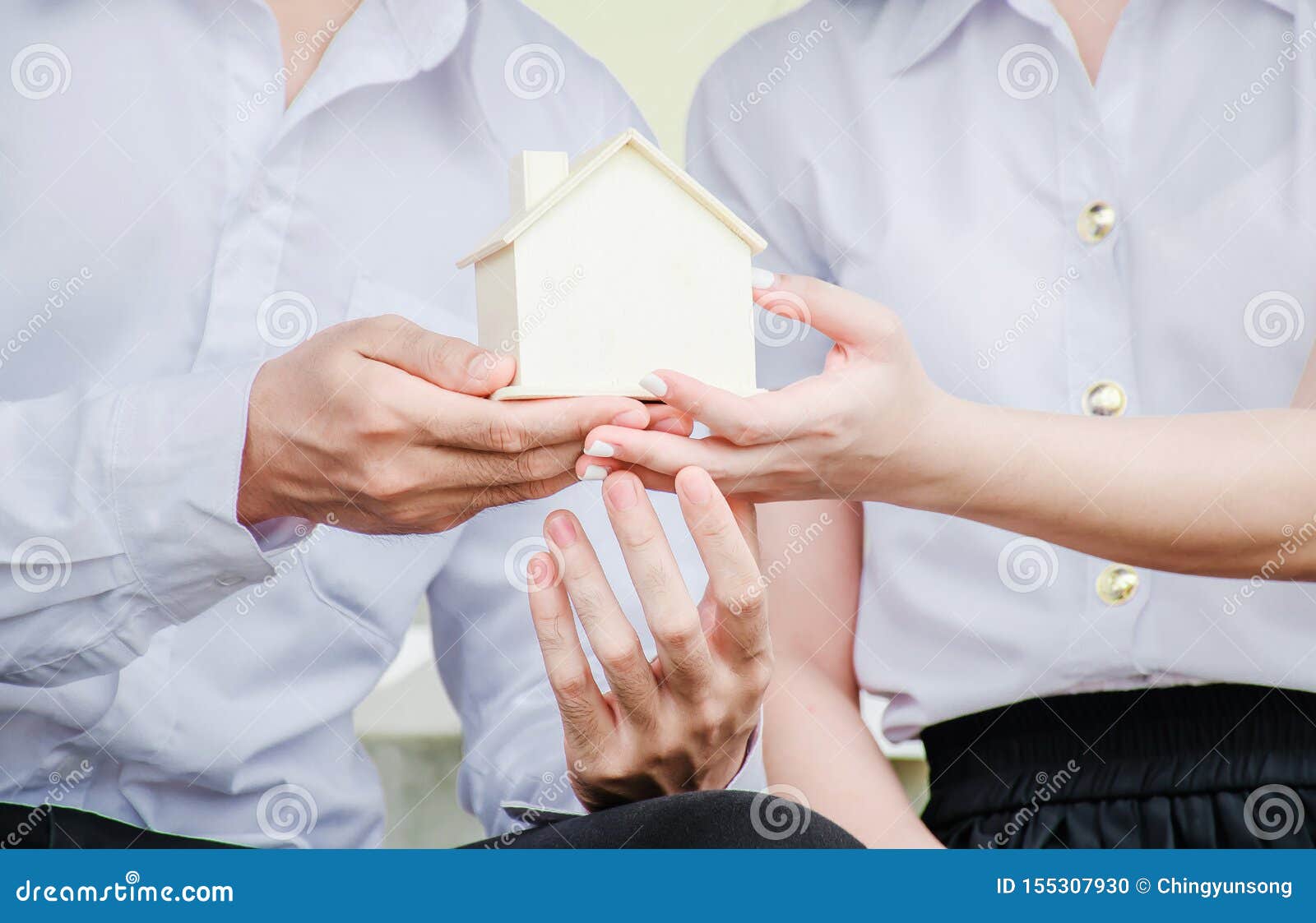 closeup hands of an couple students holding a little house together, concept of sustaining a house between two people.