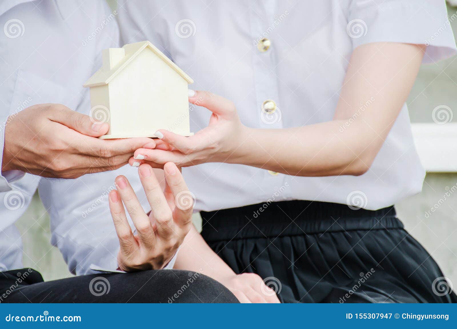 closeup hands of an couple students holding a little house together, concept of sustaining a house between two people.