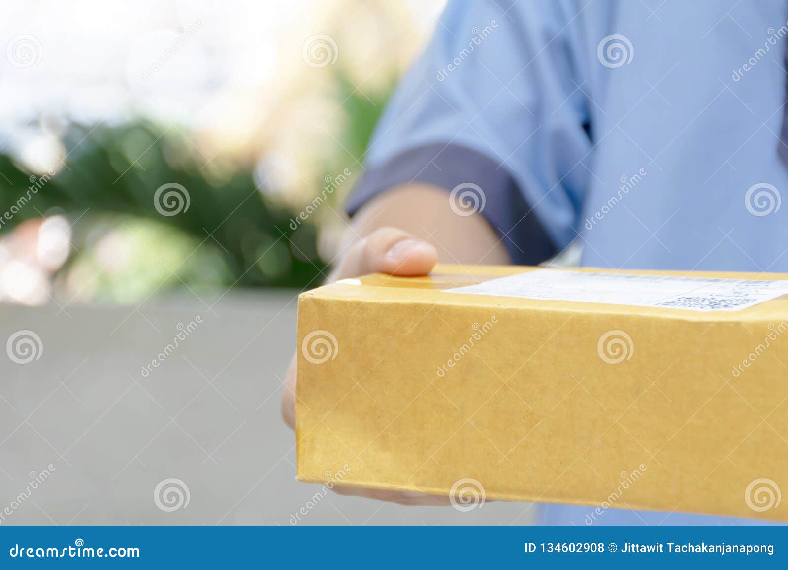 Closeup hands of delivery man holding package to deliver. Courier hand holding brown box. Detail of delivery man carrying cardboard parcel with label with copy space