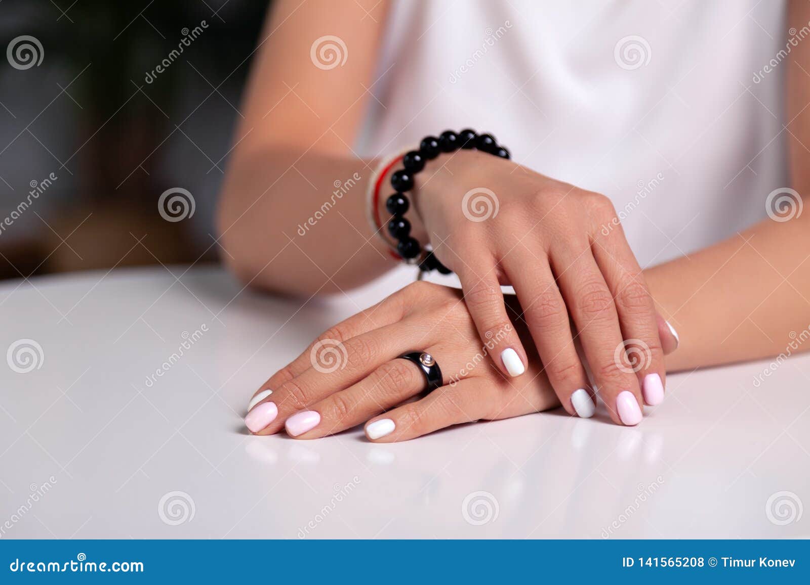 closeup model hands with manicure, white nails, black ring with stone, bracelet made of shiny black beads, red, beige braided