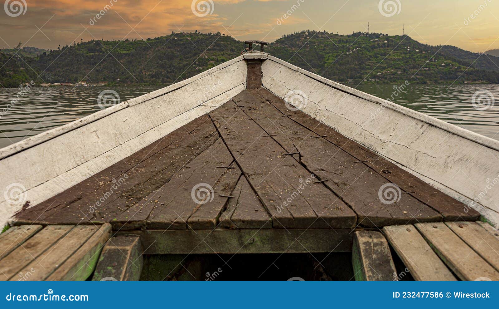 closeup of an old rough wooden boat on the water surrounded by hills during the sunset