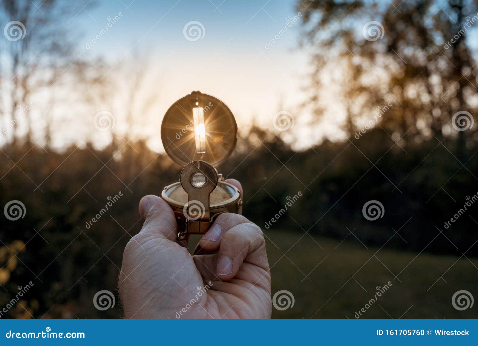 closeup of a person holding a compass with sun shining through the hole with blurred background