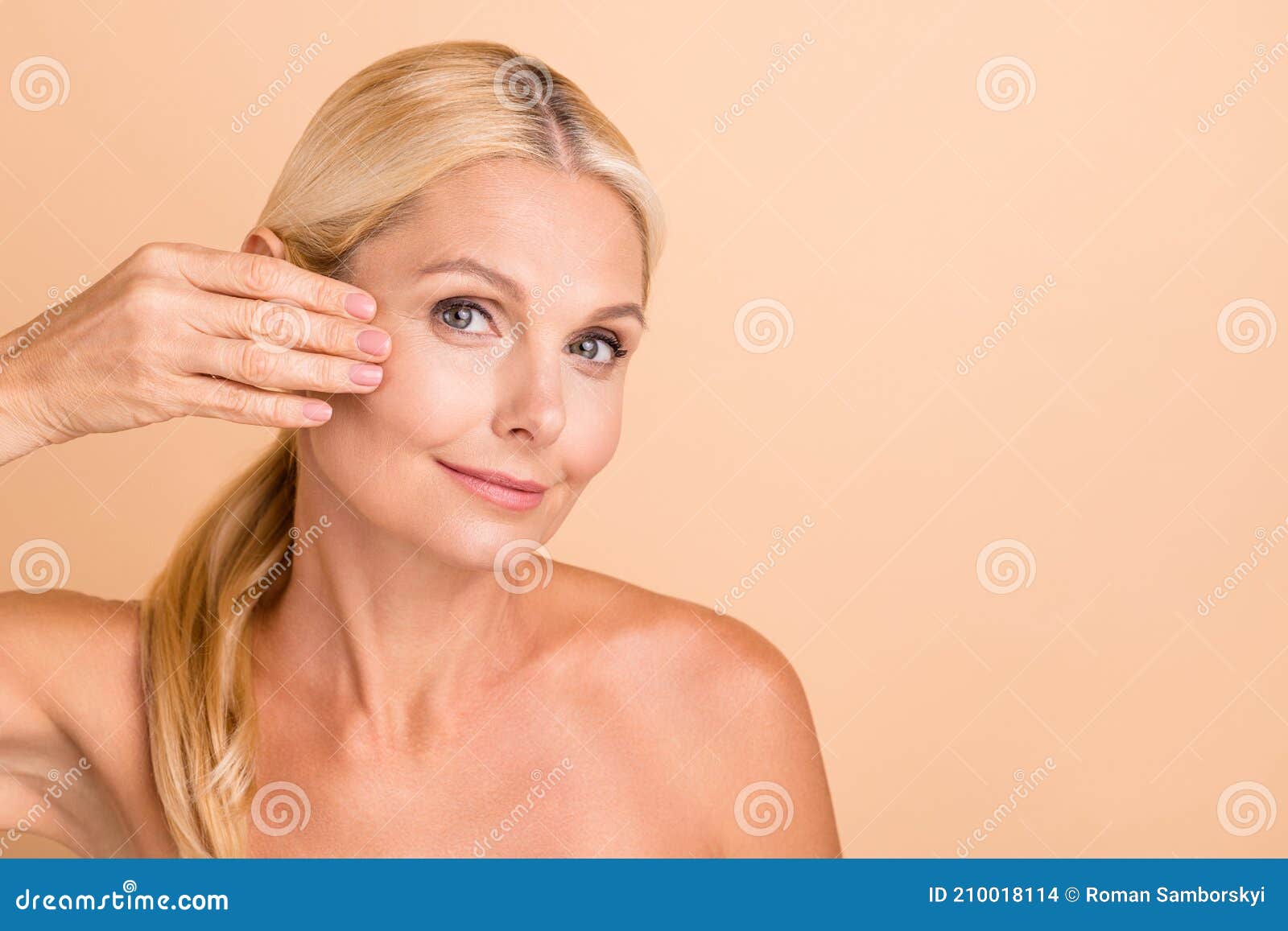 closeup photo of natural beauty aged lady nude shoulders touch fingers cheek apply anti age uplift cream  beige