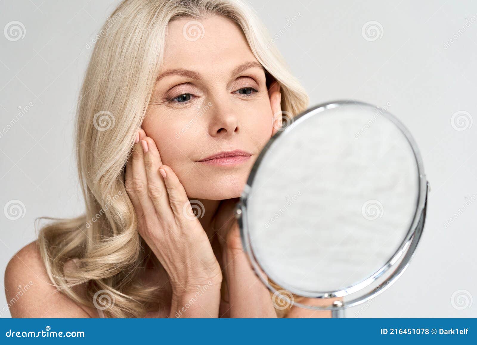 closeup portrait middle age 50 woman looking at mirror, touching healthy skin.