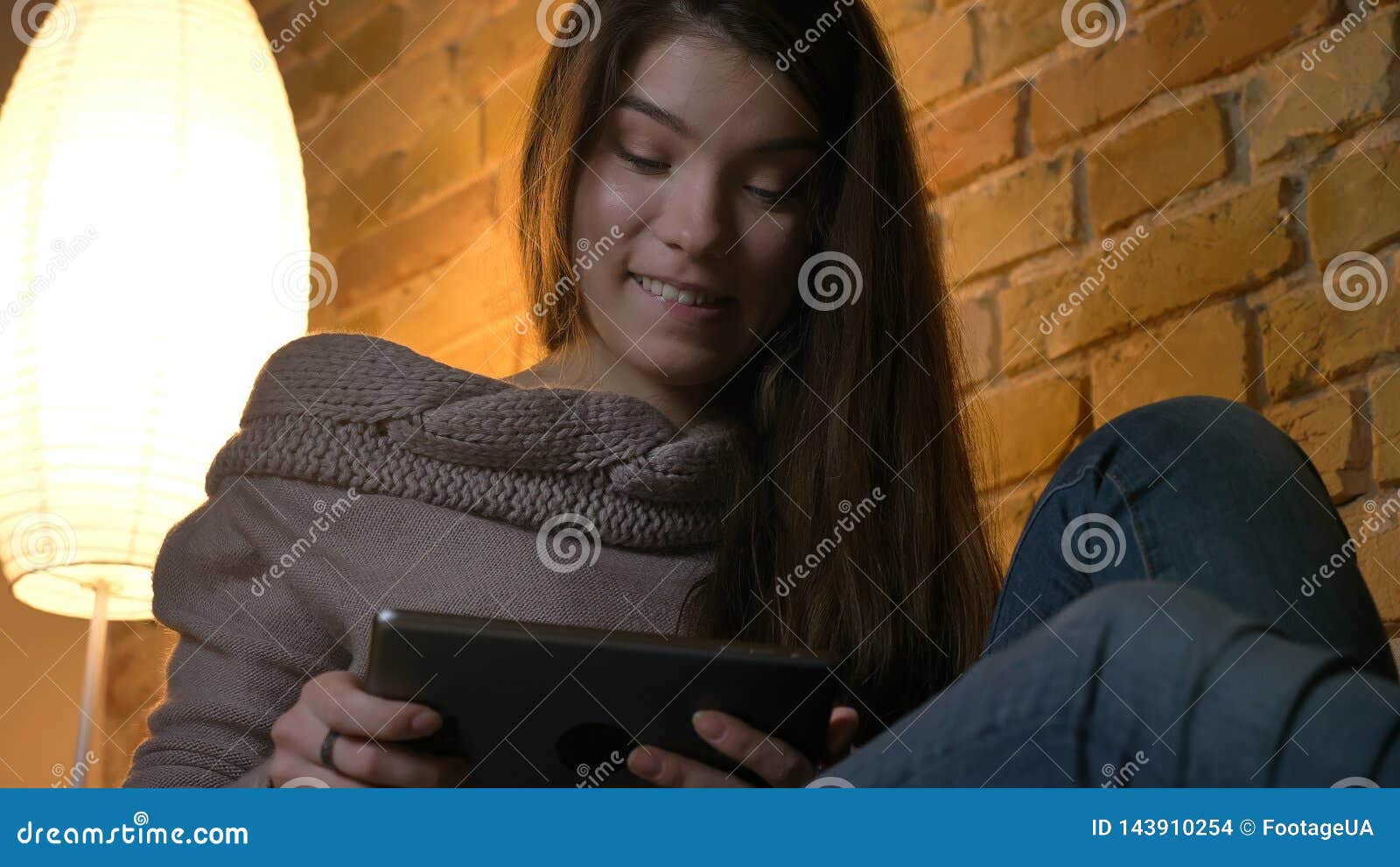 closeup portrait of young attractive caucasian female using the tablet while resting laidback on the sofa and smiling