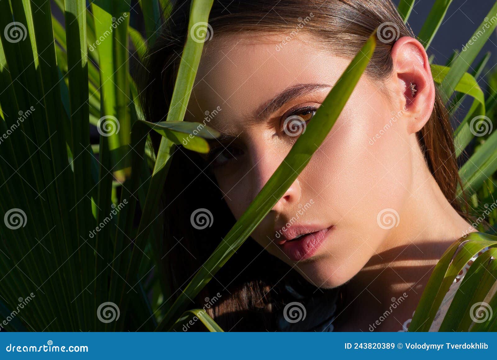 Closeup Portrait Of Young And Beautiful Woman With Perfect Smooth Tanned Skin In Tropical Leaves 