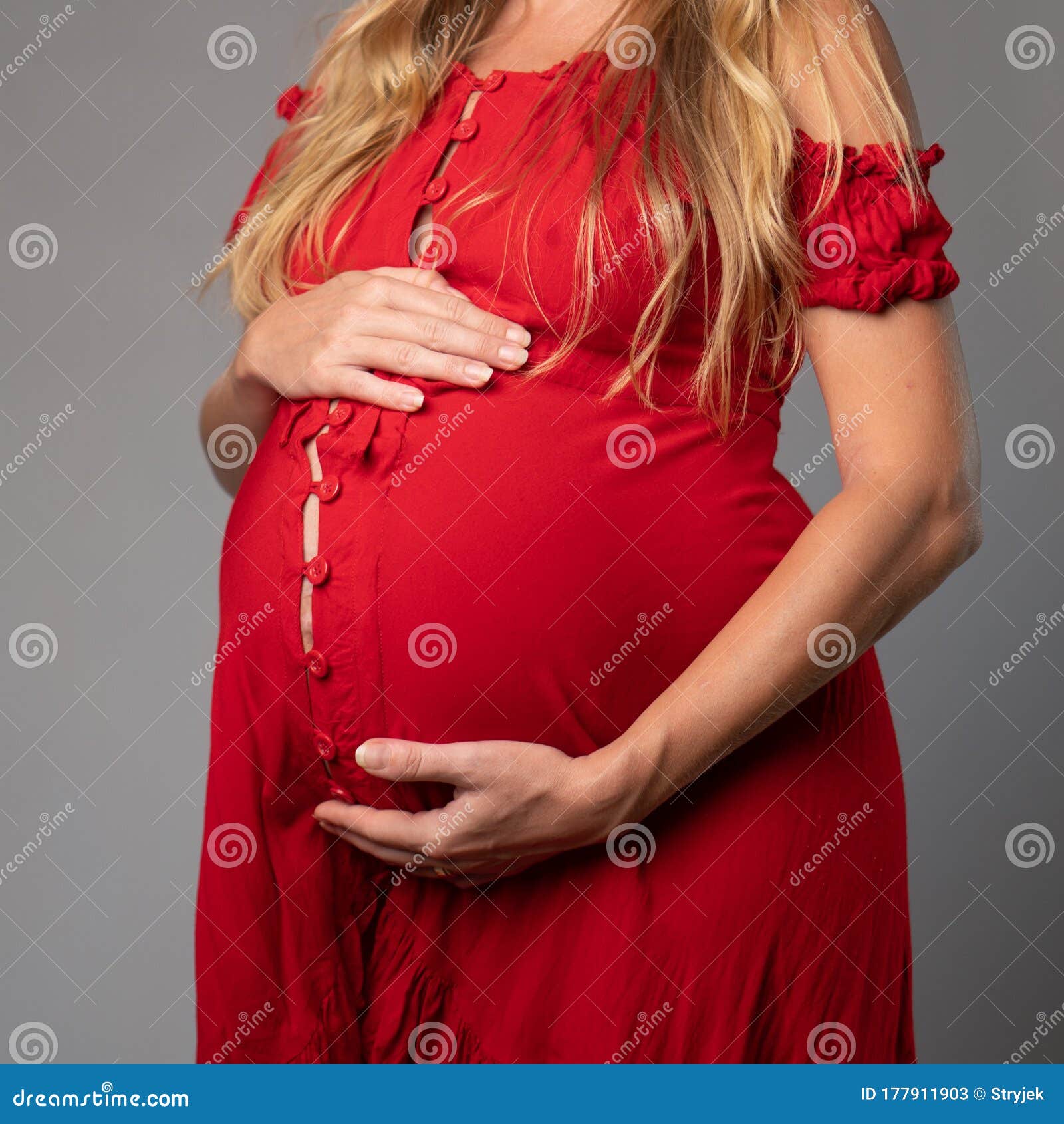 Closeup Pregnant Woman In Red Dress Holding Her Belly While Standing Over Gray Wall Background