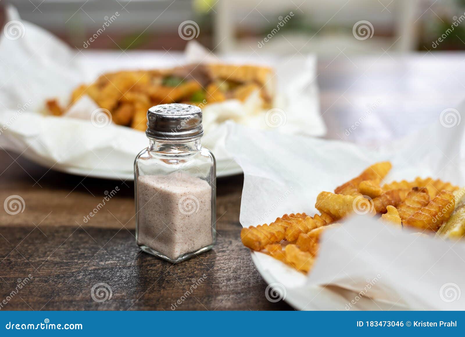 Closeup of a Salt Shaker on a Table with Takeout Food Stock Photo