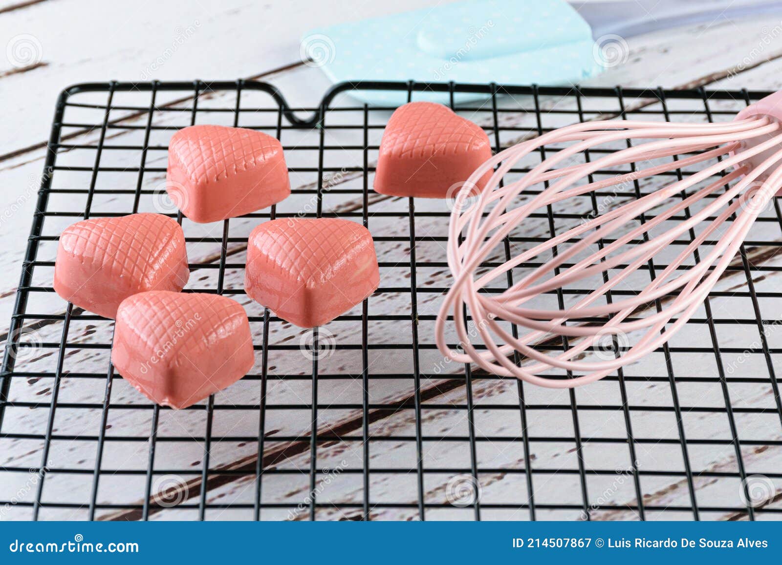 closeup of several white chocolates tinted with pink paint, on a black fence, next to a spatula and fouet