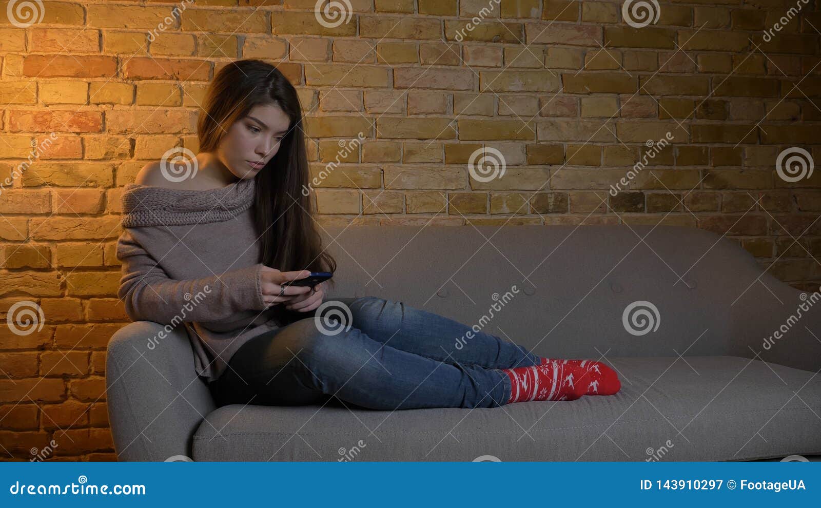 closeup shoot of young cute caucasian female messaging on the phone while resting laidback on the sofa at cozy home