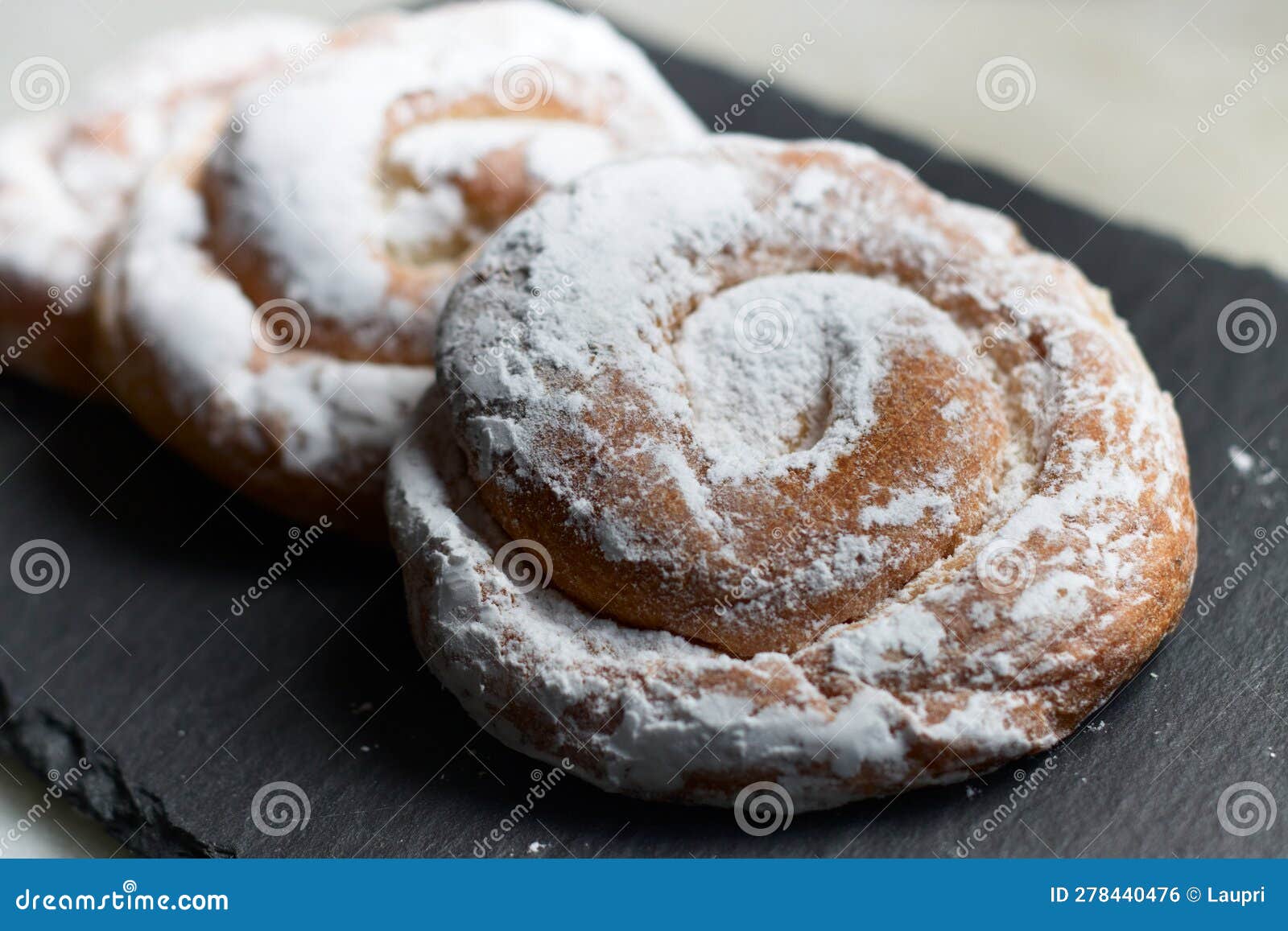 closeup of some ensaimadas with icing sugar on a slate table