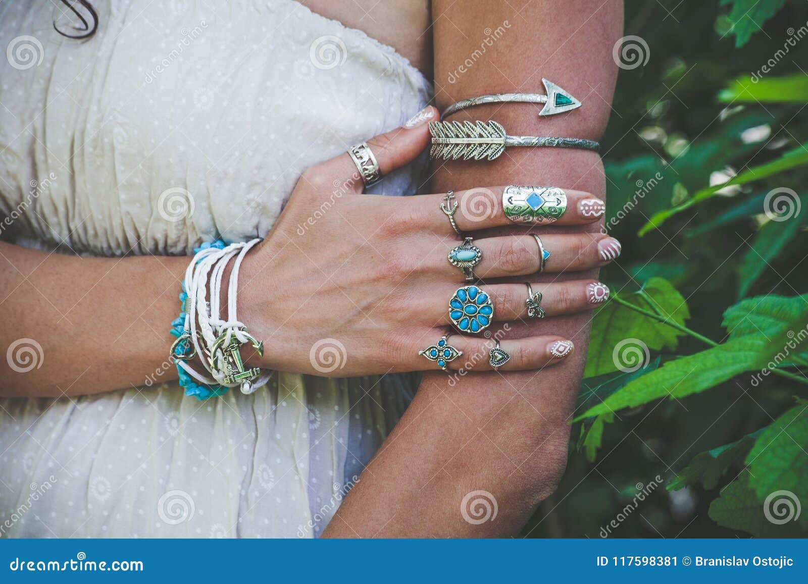 closeup of young woman hand and arm with lot of boho style jewrly, rings and bracelets outdoor shot