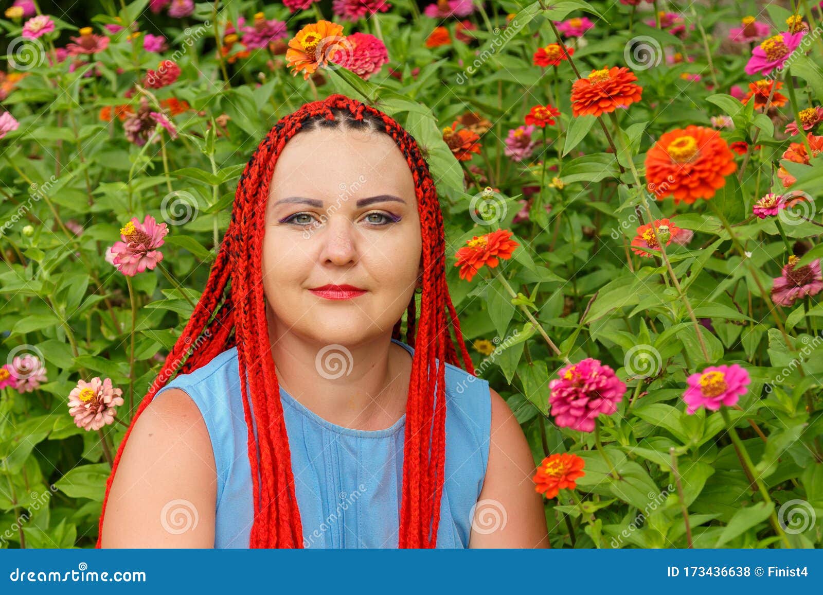 closeup of a young woman with red hair among red orange flowers.