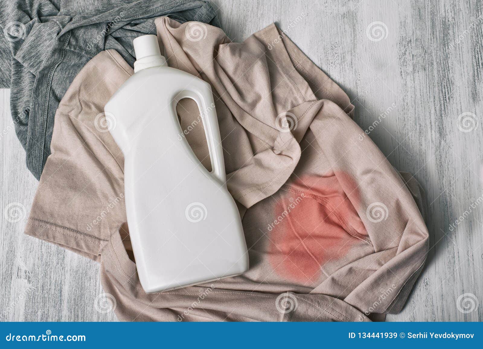 clothes with stains and a bottle of detergent. top view