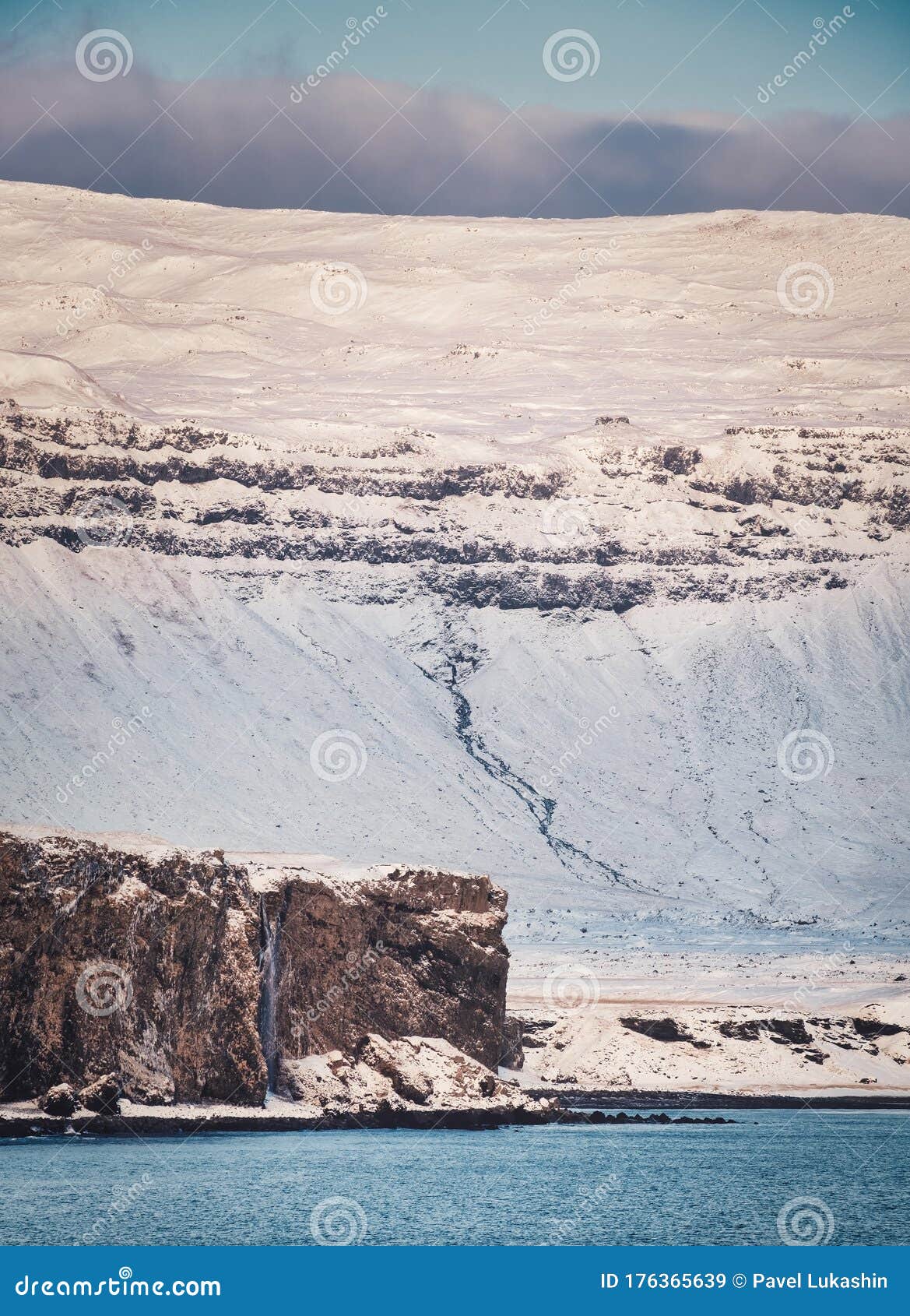 Coast of the Atlantic Ocean with a Huge Mountain in the Snow and a Cliff in Cold Iceland Winter