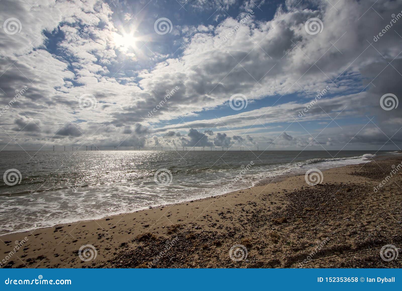 Coast. Dramatic weather sky. Offshore wind farm turbines. Coast. Dramatic weather sky landscape seascape. Offshore wind turbine farm. English coastal scene with pebbled beach and beautiful cloudy sky over sea waves with windmill turbines on the horizon