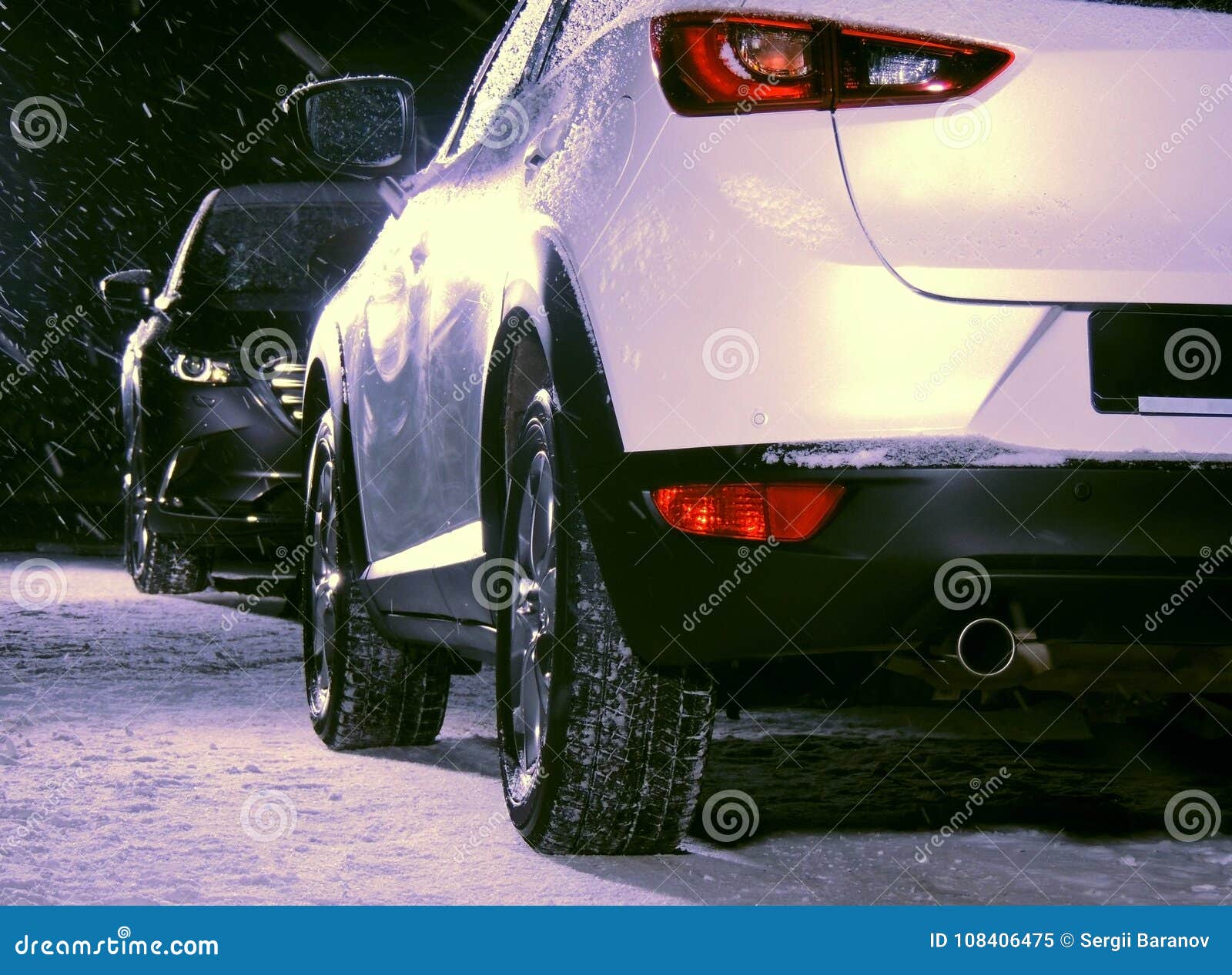Coche negro contra el coche blanco en el camino de la nieve en la noche. Coche blanco enfrente del coche negro en la noche en el camino nevoso
