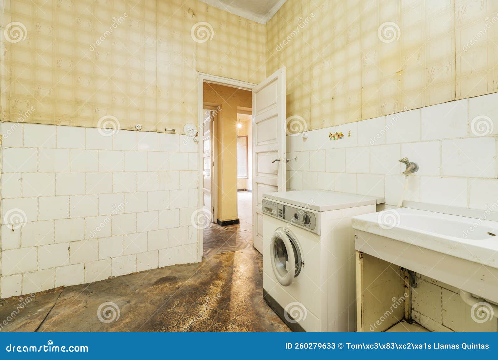 cocina vieja, sucia y destartalada con suelo oscuro, azulejos blancos y papel amarillo en las paredes