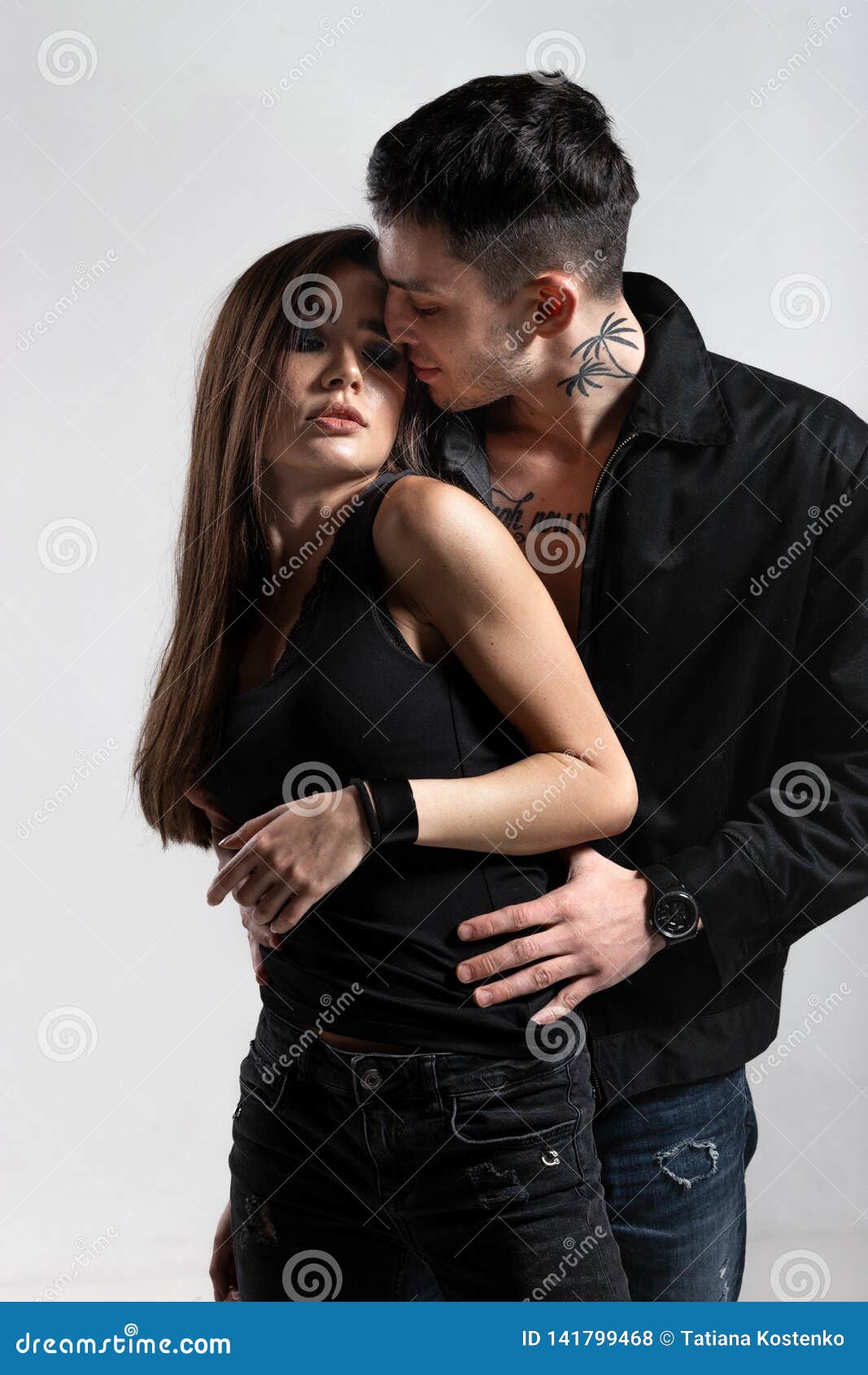 Cocky Guy in Black Jacket on a Naked Torso is Hugging from Behind a Brunette Girl Dressed in a Black T-shirt and Jeans Stock Photo