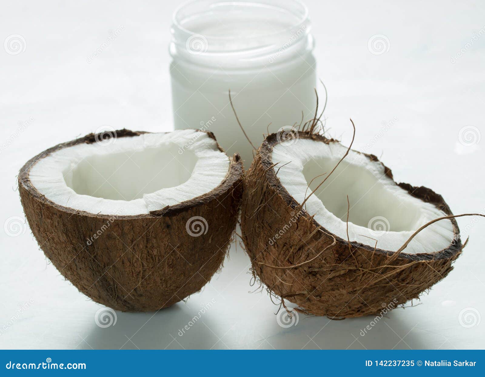 Coconut Oil in a Jar and Coconut Halves on the Table Stock Image