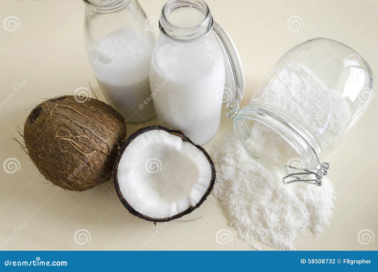 Coconut products. Cracked open coconut with meat cut in half, grounded flakes in a mason jar, flour and fresh milk in glass bottles on a table with red ruby background.