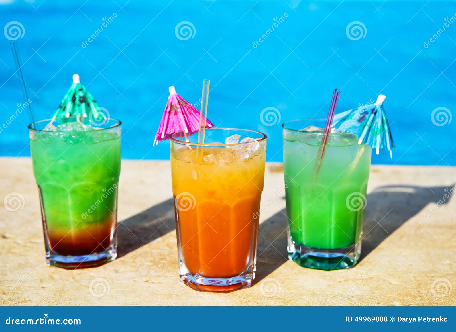 Colored cocotail drinks by tropical swimming pool