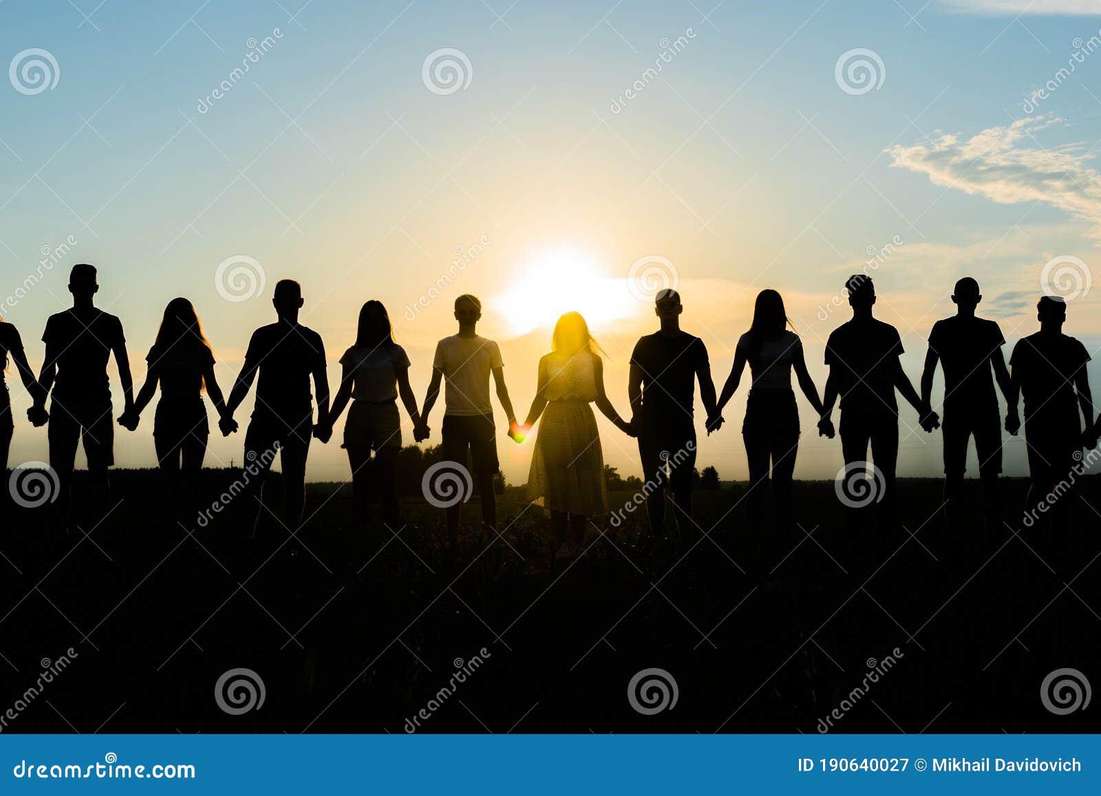 cohesion concept. black silhouettes of friends holding hands stands at sunset.