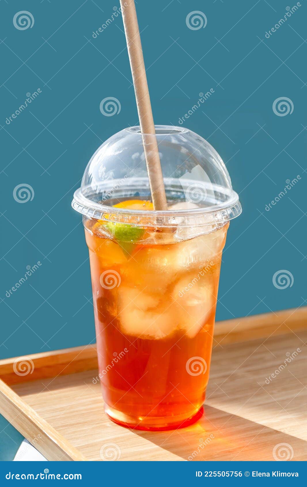 Cold Fruit Tea with a Ice in a Plastic Cup with a Lid on a Wooden