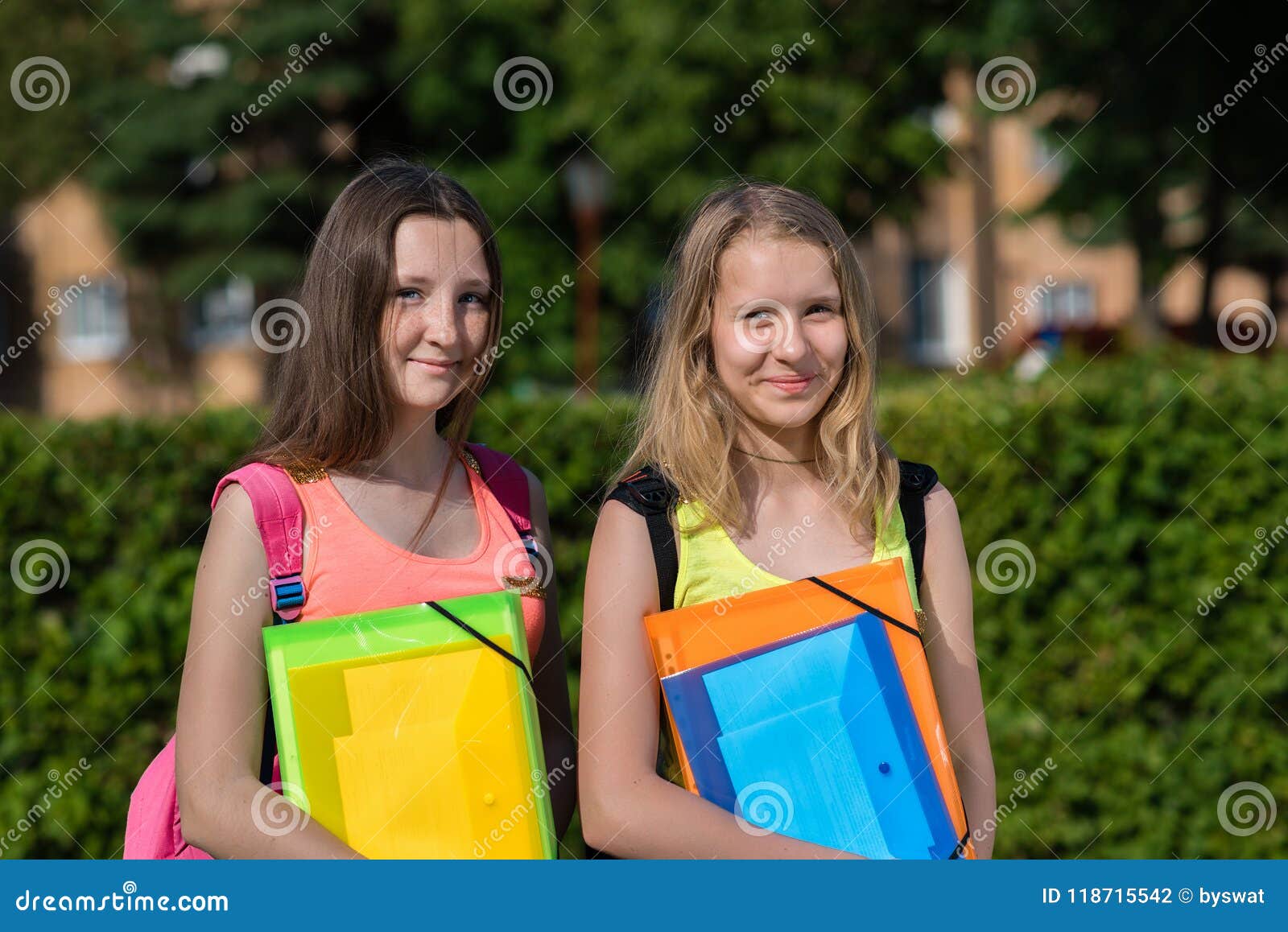 Colegiala de dos muchachas Verano en naturaleza Sonrisa feliz Aliste para las lecciones de la escuela En manos de una carpeta con. Colegiala de dos muchachas Verano en naturaleza Sonrisa feliz Aliste para las lecciones de la escuela En las manos de una carpeta con los cuadernos Él descansa después de escuela Las mejores novias