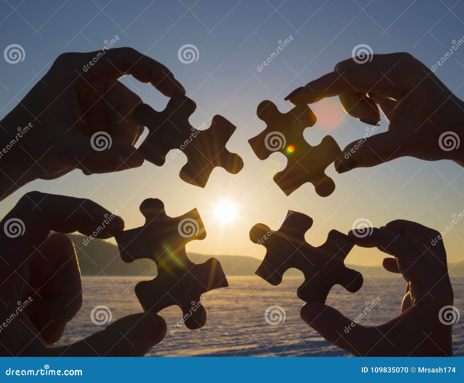 collaborate four hands trying to connect a puzzle piece with a sunset background.