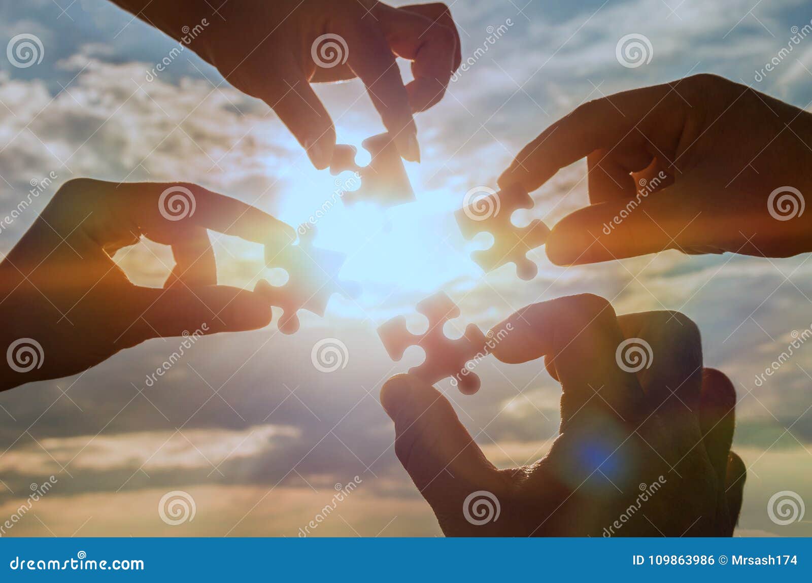 collaborate four hands trying to connect a puzzle piece with a sunset background.