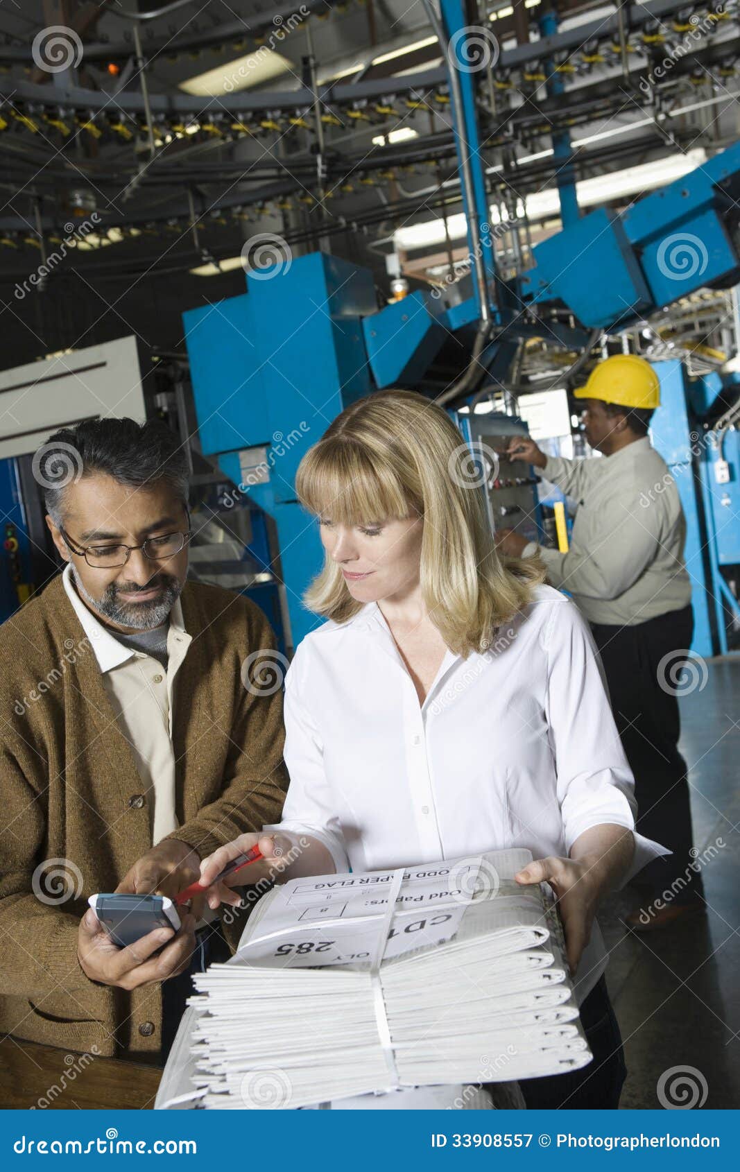 Colleagues with Calculator Checking Newspaper in Factory Stock Image