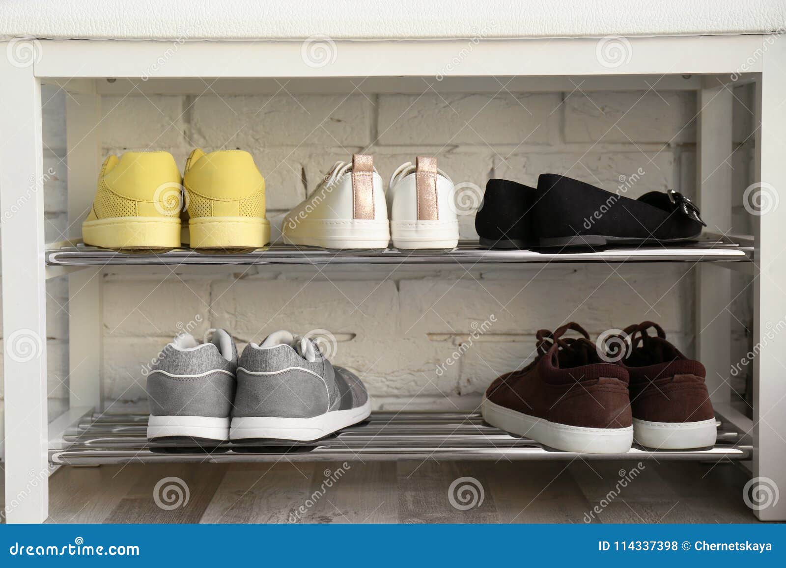 Collection of stylish shoes on rack storage near white brick wall