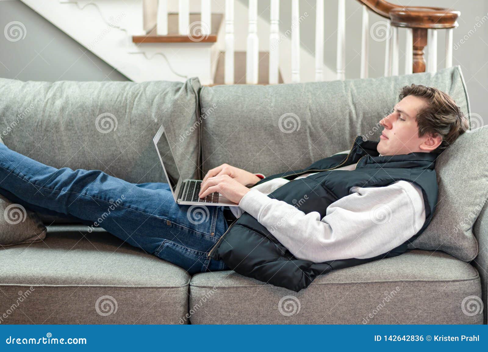 College Student Using Laptop while Laying on the Couch Stock Photo