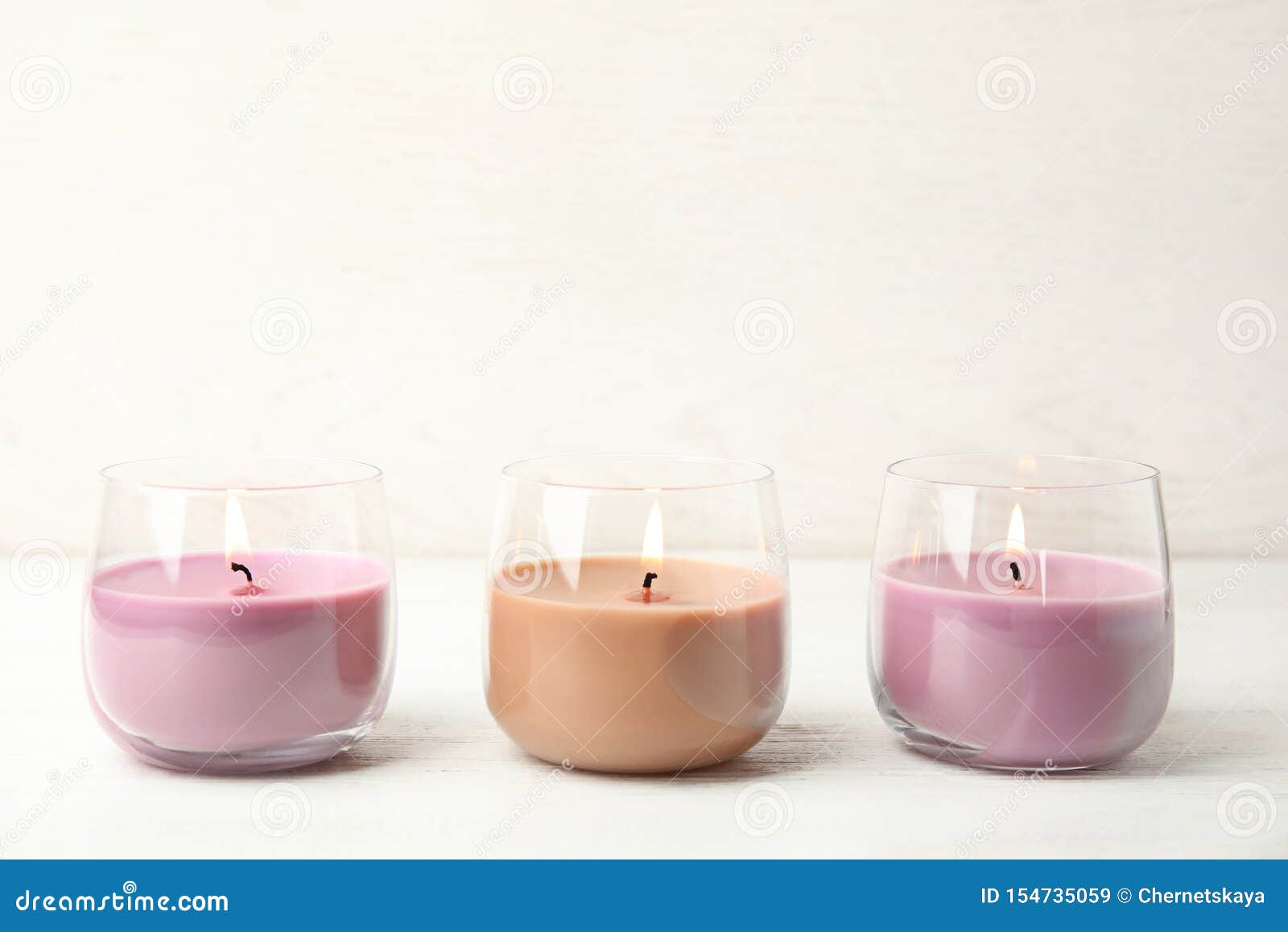 Color Wax Candles in Glass Holders on White Table, Space for Stock