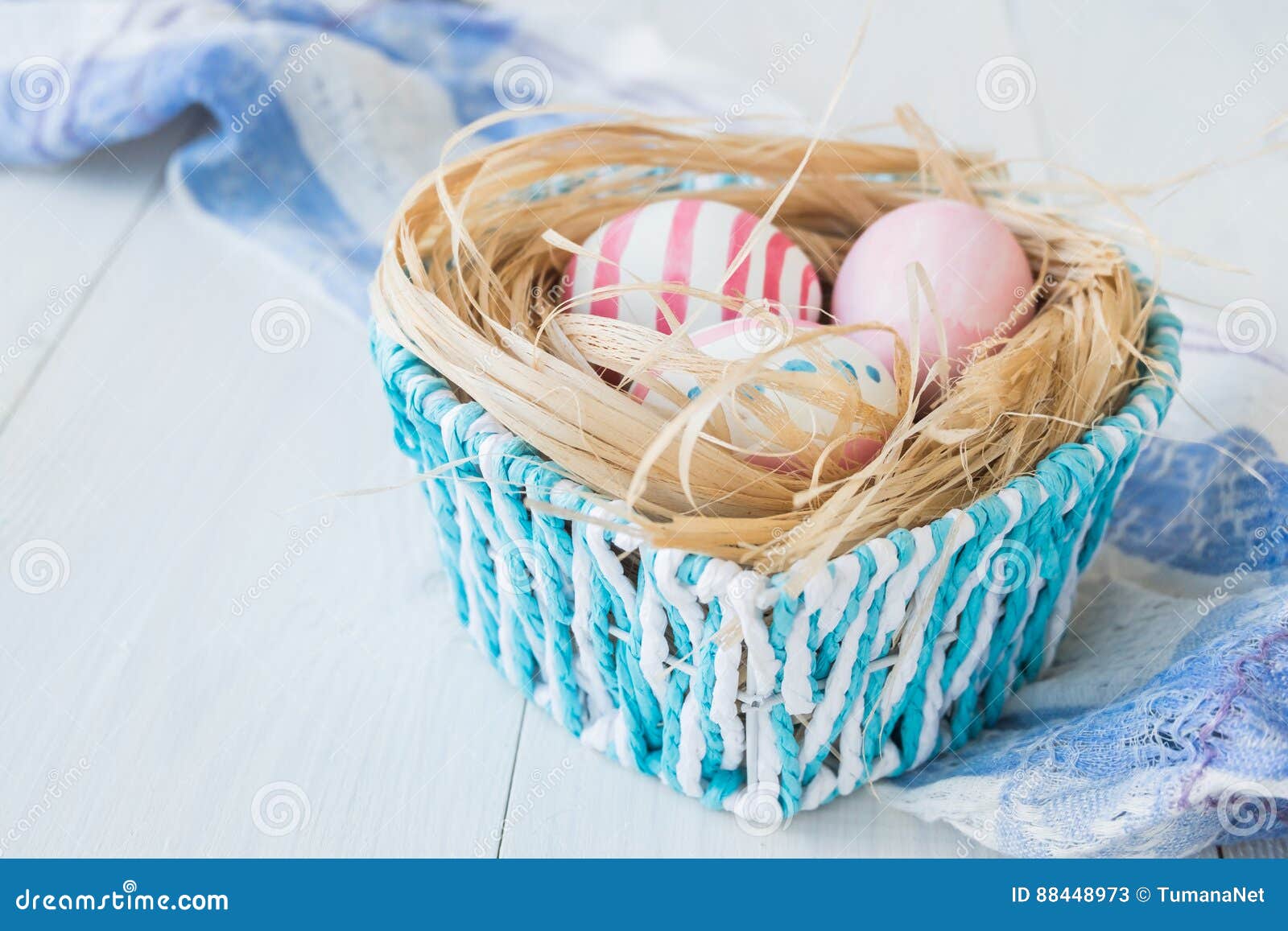 colorful easter eggs on the white rustic wooden background with nest and blue basket on the linen towel selective focus.