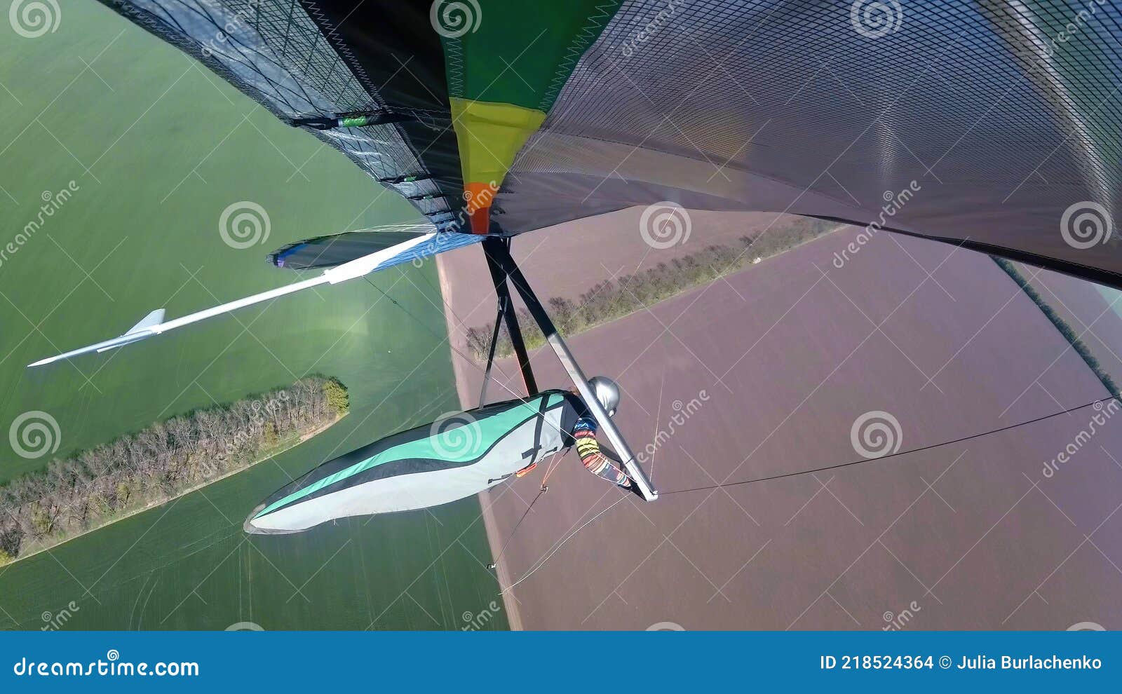 colorful hangglider wing soars above green cultivated fields