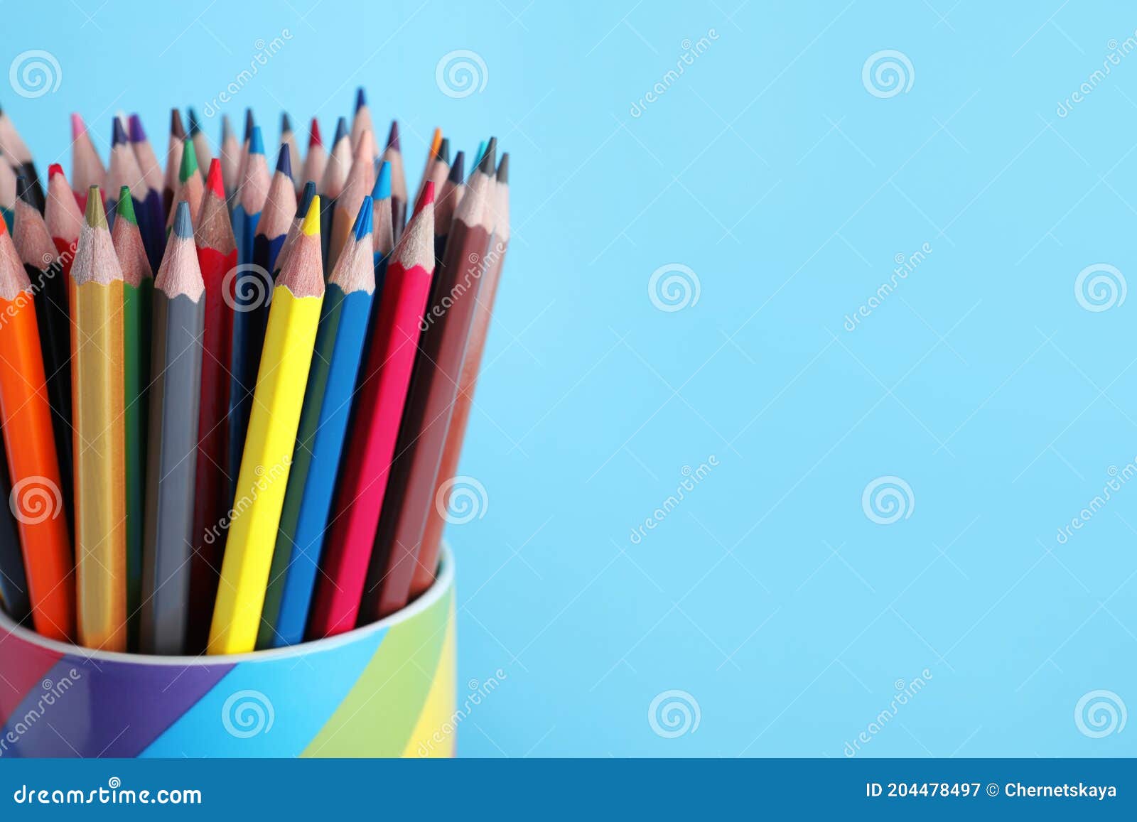 Colorful Pencils in Cup on Light Blue Background, Closeup. Space for