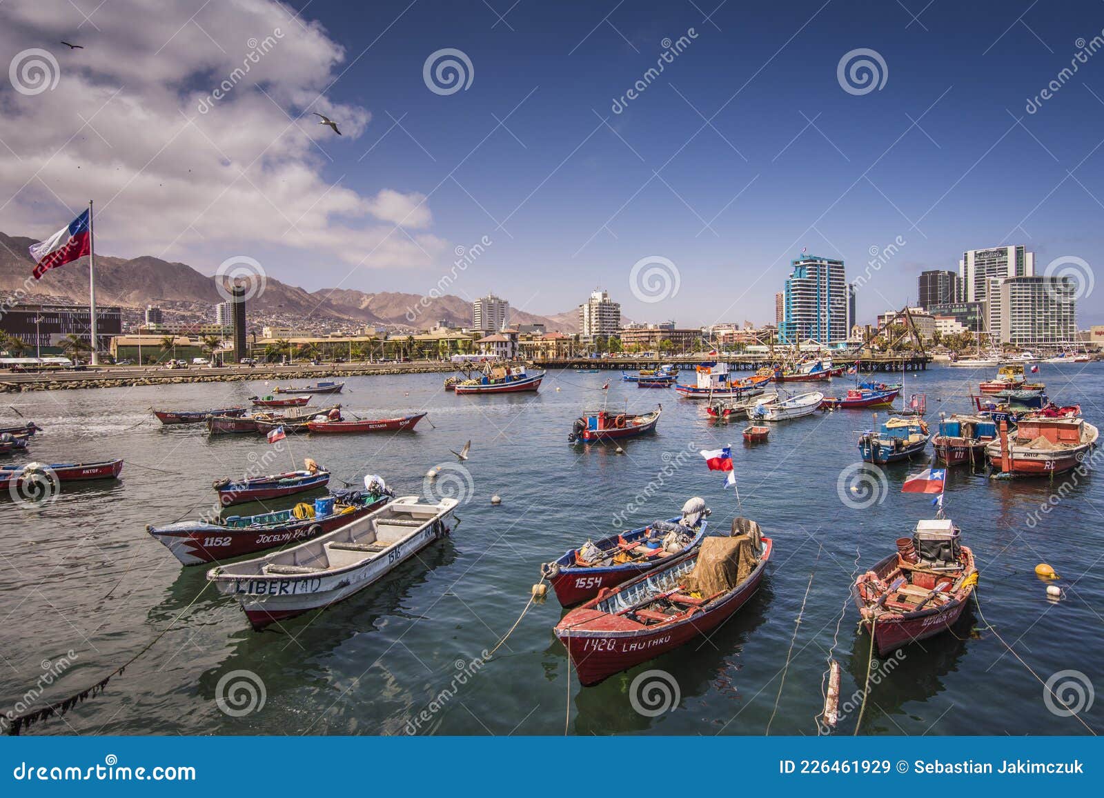 colourful botes anchored at antofagastaÃÂ´s harbour and the chilean flag in the left. antofagasta city at the background.