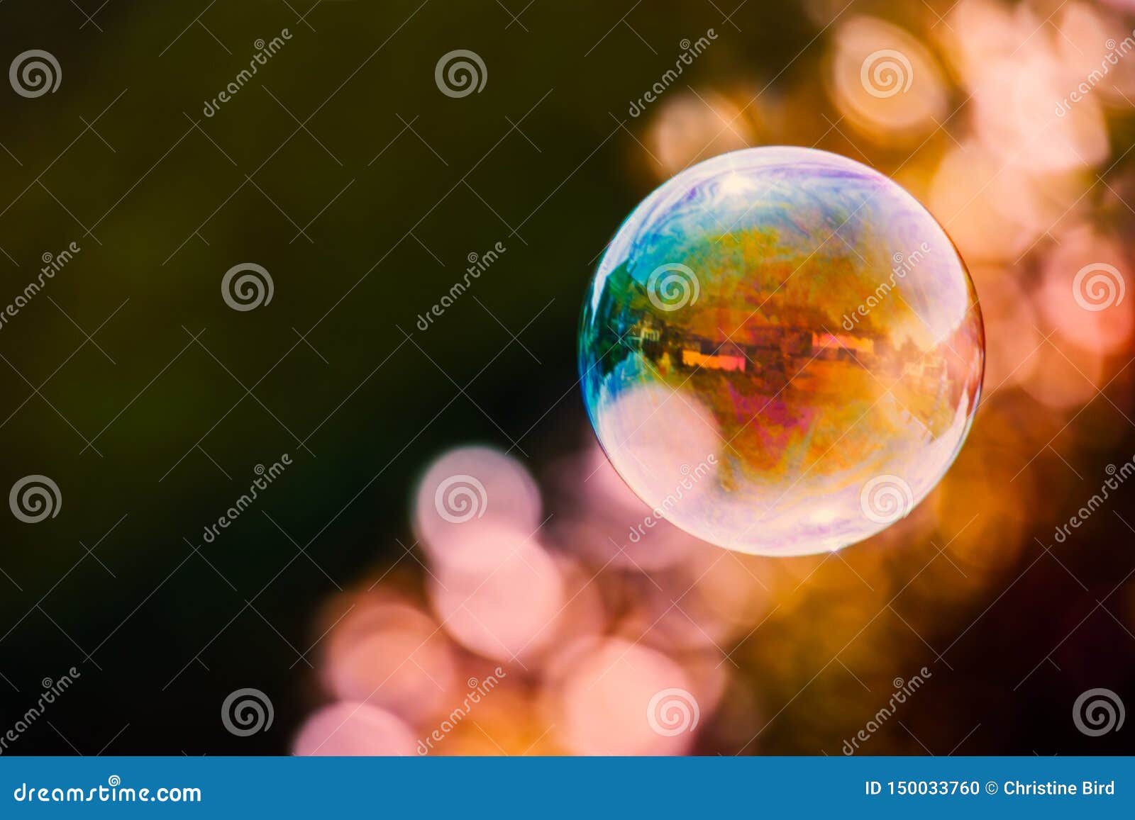 colourful soap bubble floating against a mainly dark background with a streak of light bubble bokeh.