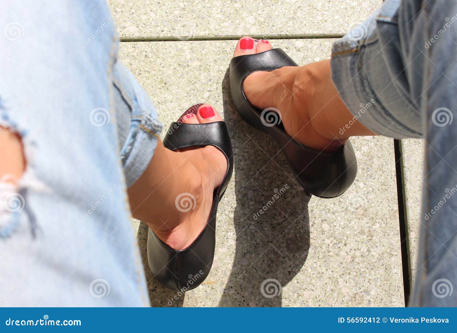 Young woman wearing a blue top, black jeans and high heels posing in front  of a gray stone wall Stock Photo - Alamy
