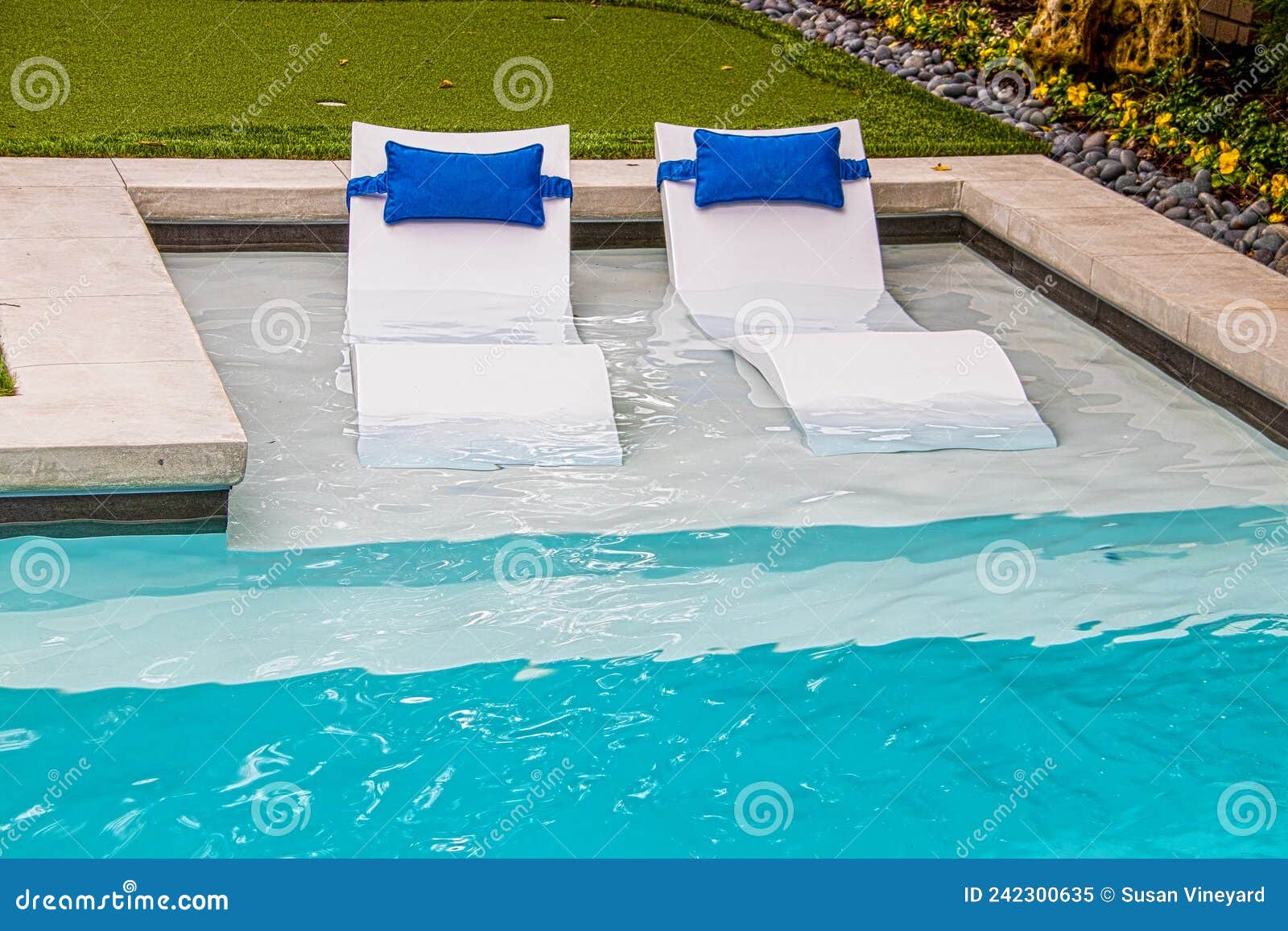 comfy white loungers in shallow end of refreshing blue swimming pool in yard with flower trim around the edge