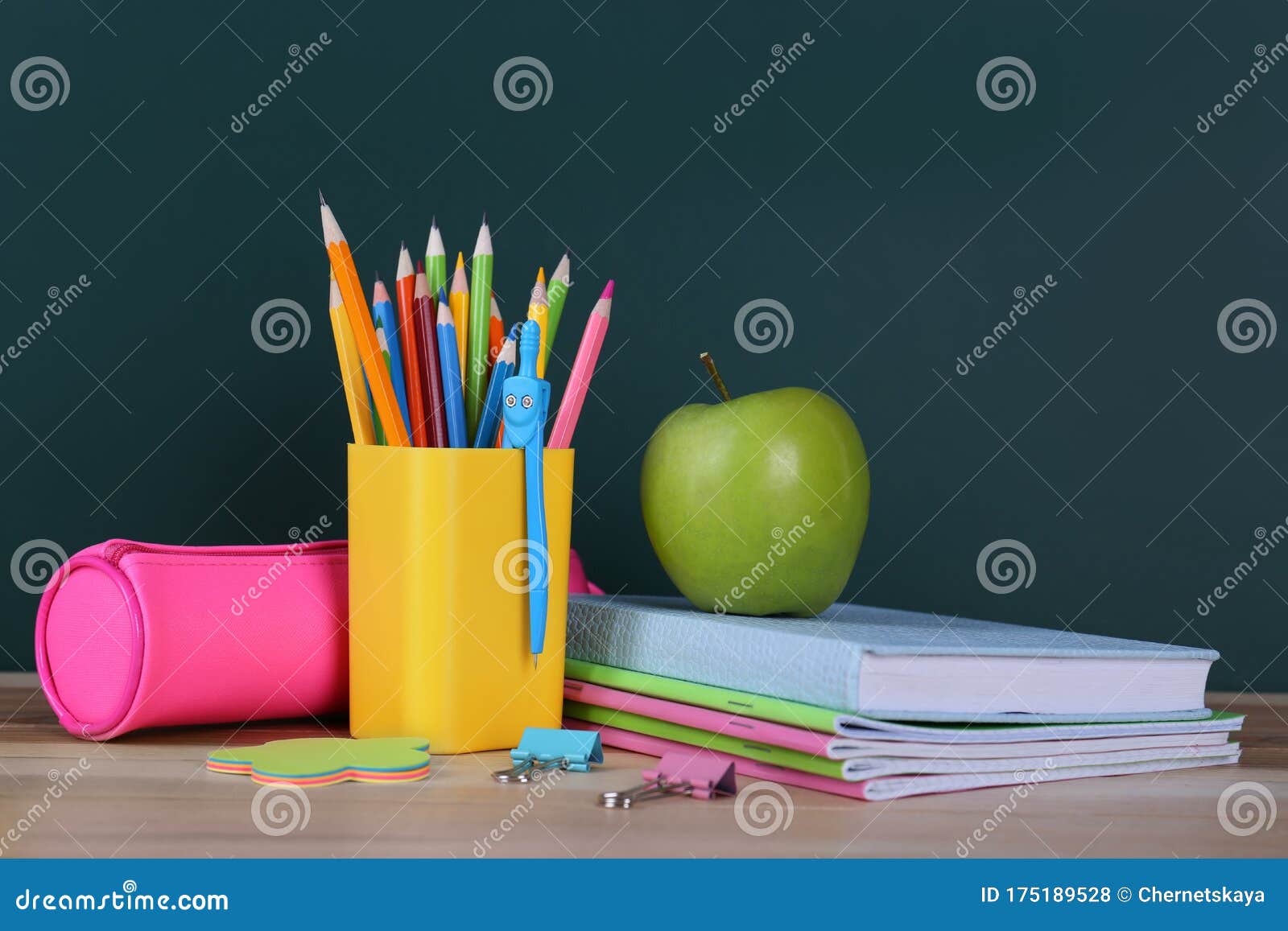 Composition with Stationery and Apple on Table Near Chalkboard. Doing Homework Stock Photo