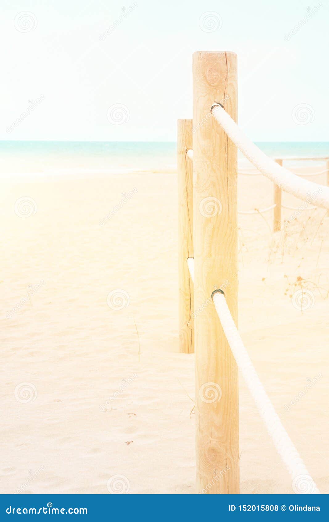 Summer travel vacation concept. White pinkish beach sand turquoise ocean blue sky. Tranquil idyllic scene. Rope railing with wooden poles. Lifestyle image with copy space. Vertical