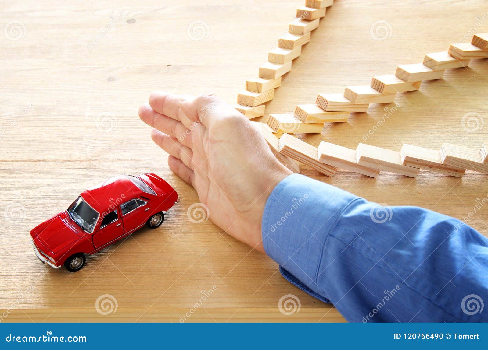  A hand stopping dominoes from falling with a red toy car behind them, representing car insurance protection.