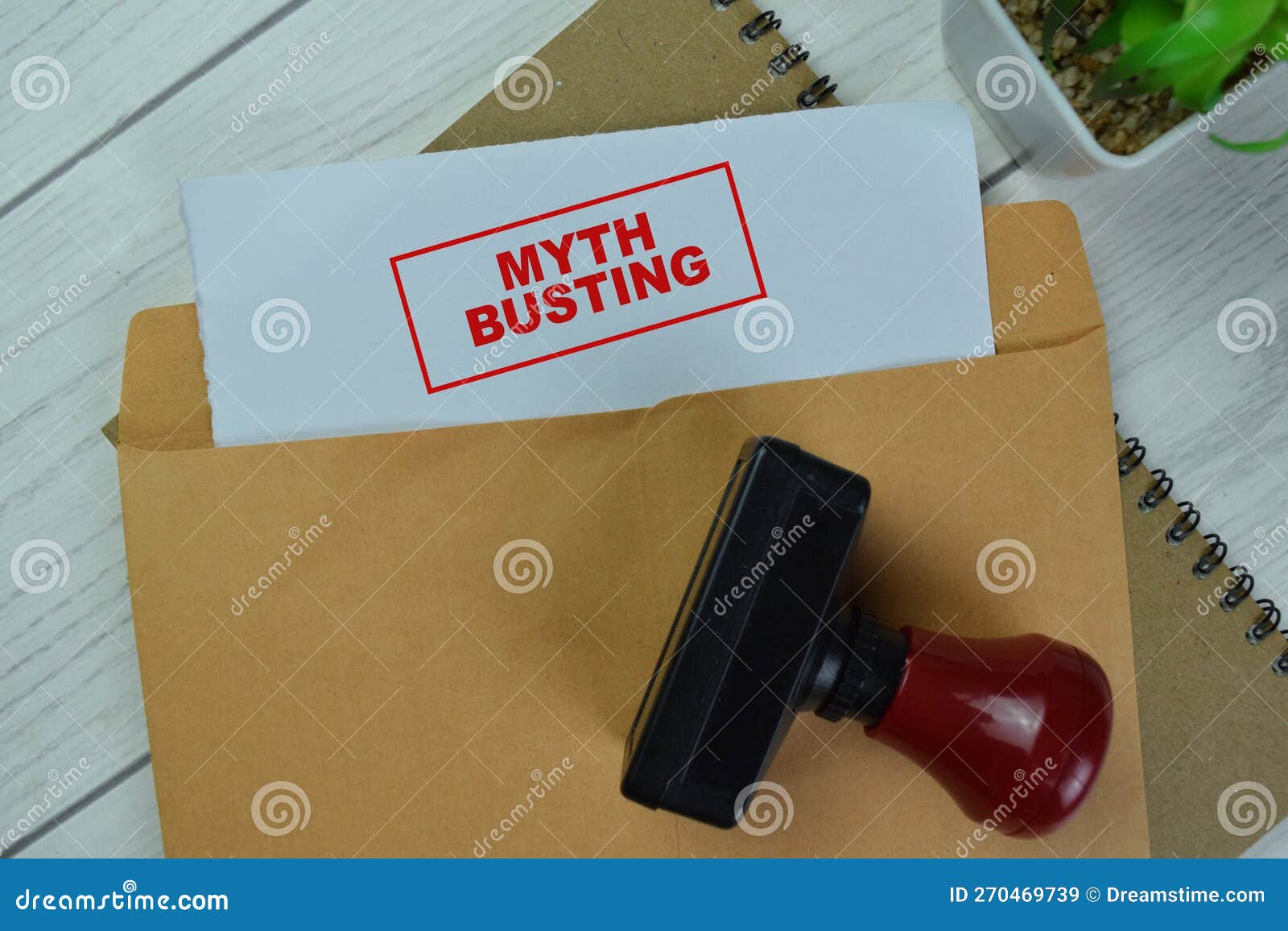 concept of red handle rubber stamper and myth busting text above brown envelope  on on wooden table