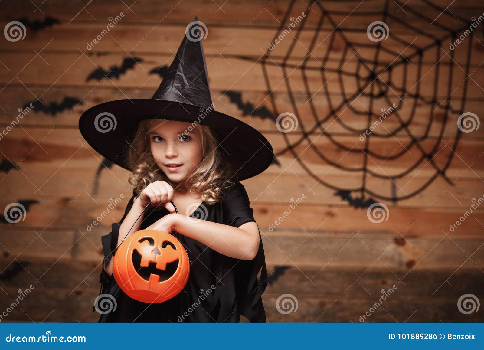 Concepto de la bruja de Halloween - el pequeño niño caucásico de la bruja goza con el tarro de la calabaza del caramelo de Halloween sobre fondo del web del palo y de araña